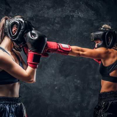 Process of fight between two female boxers in gloves and helmets over dark background.